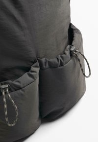 Sac en nylon noir avec une surface texturée, fermeture à cordon, et deux poches froncées avec des détails de cordon ajustable.