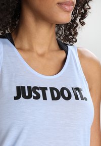 Světlomodrý atletický nátělník z měkké látky s černým potiskem sloganu „JUST DO IT.“ Má kulatý výstřih a tenká ramínka.