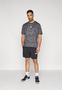 Hallikashallane tie-dye lühikeste varrukatega T-särk, millele on lisatud mustad lühikesed püksid valgete triipude ja Adidas logo. Stiili lõpetavad spordijalatsid.