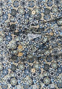 Buttoned shirt with blue, green, and beige floral patterns and close-up of the cuff showing two buttons and detailed stitching.