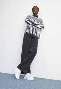 Svart och vit randig långärmad skjorta, i kombination med mörkgrå vida byxor och vita sneakers. Enkel, avslappnad design.