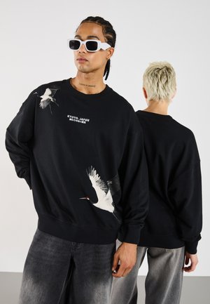 Black oversized sweatshirt featuring a white crane graphic on the front and the text "KYOTO, JAPAN," with ribbed cuffs and hem.
