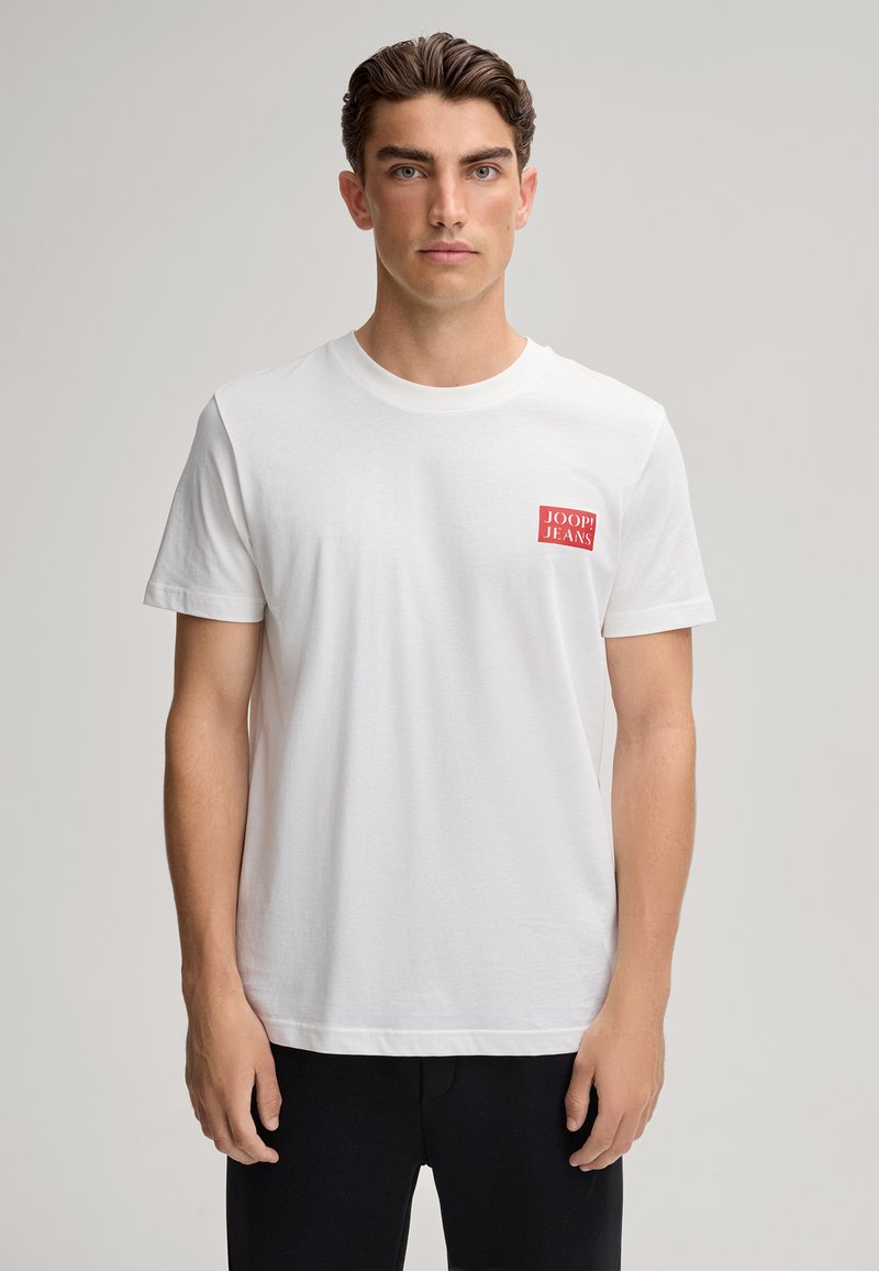 Biała bawełniana koszulka z okrągłym dekoltem i krótkimi rękawami. Posiada czerwony kwadratowy logo na lewej piersi. Prosty fason, luźny krój.