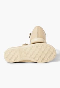 Beige Leinenschuh mit runder Zehenpartie, strukturiertem Sohlenprofil und verstellbaren Schnallen an der Seite. Flache Gummisohle für besseren Halt.