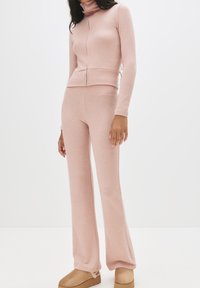 Set da lounge in maglia rosa composto da un dolcevita aderente e pantaloni svasati. Texture morbida, dettagli a coste e design minimalista.