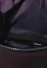 Lilla inderstof i en taske, med en lynlåslomme og en sort mærkat med teksten "Desigual". Glat tekstur, elegant design.