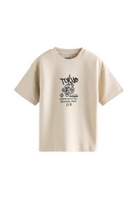 T-shirt beige a maniche corte in tessuto testurizzato, con stampa grafica nera di una tigre e testo che include "TOKYO." Motivo a griglia quadrata.
