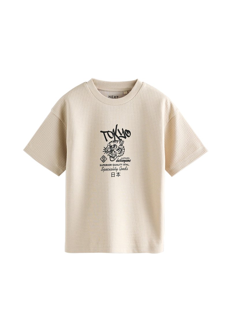 T-shirt beige a maniche corte in tessuto testurizzato, con stampa grafica nera di una tigre e testo che include "TOKYO." Motivo a griglia quadrata.