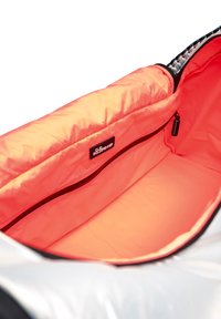 Sac isolé argenté avec un intérieur orange vif ; comprend une poche zippée et une étiquette en tissu. Texture lisse, forme arrondie.