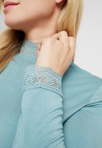 Light blue long-sleeve top featuring intricate lace trim on the collar and cuffs, with a smooth, soft texture and fitted design.