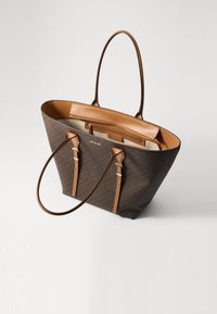 Torba typu tote w brązowym materiale z monogramem, z jasnobrązowymi skórzanymi akcentami, zamknięciem na zamek błyskawiczny na górze, dwiema długimi uchwytami oraz wewnętrzną kieszonką na zamek.