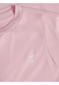 Różowa koszulka sportowa z okrągłym dekoltem, gładką fakturą i białym logo w kształcie chevronu po lewej stronie. Posiada siateczkowe wstawki zapewniające wentylację.