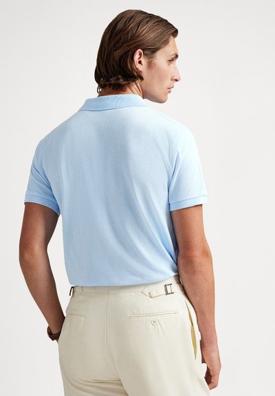 Svetlomodré polo tričko s textúrovanou látkou, krátkymi rukávmi a golierom. Kombinované s béžovými nohavicami so zadnými vreckami a detailmi na pracke.