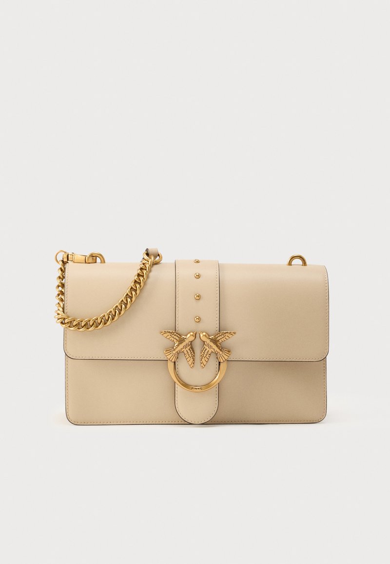 Μπεζ δερμάτινη τσάντα χειρός με χρυσή αλυσίδα, με διακοσμητικό κούμπωμα που απεικονίζει δύο πουλιά και τρουκς στην πρόσοψη. Ορθογώνιο σχήμα.