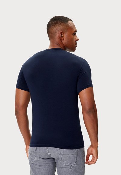 Granatowy t-shirt z krótkim rękawem, materiał bawełniany, okrągły dekolt, dopasowany krój, gładka faktura, noszony z szarymi jeansami, widoczny od tyłu.