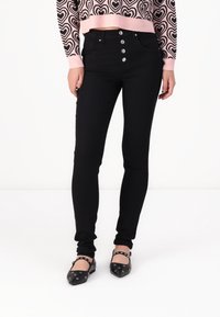 Jeans negros de cintura alta con cierre de cinco botones, diseño ajustado y ligero estiramiento. Llevados con un suéter corto de rayas con corazones rosas.