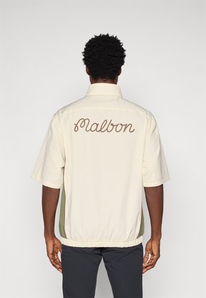 Korte mouwen jas in crème, met een lichtgroene paneel aan de zijkanten en "Malbon" in bruin geborduurd op de achterkant. Elastische tailleband.