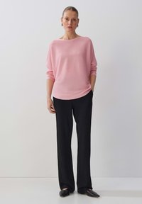 Pull en tricot rayé rose avec un large col bateau, porté avec un pantalon noir à jambes larges et des chaussures noires à bout pointu, sur un fond clair.