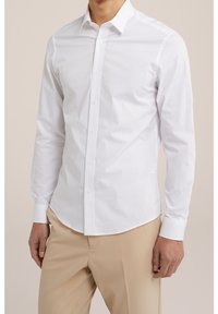 White long-sleeve button-up shirt made of cotton, featuring a structured collar, slim fit, and plain design; sleeves are buttoned at cuffs.