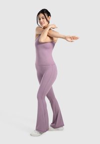 Set di abbigliamento sportivo lavanda composto da un top aderente e leggings a palazzo, realizzato in tessuto elastico per comfort e flessibilità. Scarpe sportive bianche.