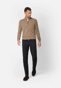 Bruine gebreide trui met een ritssluiting bij de kraag, gecombineerd met donkere broeken. Draagt donkere bruin suède schoenen. Eenvoudig, casual ontwerp met een getailleerde pasvorm.