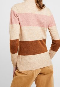 Stickad tröja med horisontella ränder i ljusbeige, rosa och brun. Mjuk textur med hög hals och ribbade muddar.