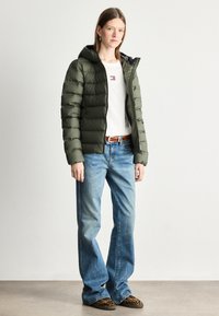 Chaqueta acolchada verde oliva con capucha, con un interior negro en contraste. Combinada con jeans acampanados de color azul claro y zapatos de animal print.