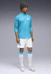 Vaaleansininen pitkähihainen pelipaita, jossa on oransseja pilkkuja, valkoiset shortsit ja polvimittaiset sukat. Sisältää Puma-logon ja Marseille-embleemin.