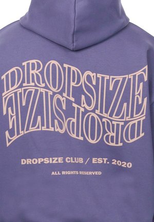 Sudadera púrpura con gran texto al revés en beige: "DROPSIZE", con "DROPSIZE CLUB / EST. 2020" abajo. Textura de tejido suave, ajuste estándar.