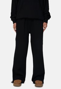 Zwarte sweatshirt met een voorzak en losse zwarte joggingsbroek. Geweven, zacht materiaal; de broek heeft een reliëflogo-detail.