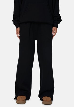 Zwarte sweatshirt met een voorzak en losse zwarte joggingsbroek. Geweven, zacht materiaal; de broek heeft een reliëflogo-detail.