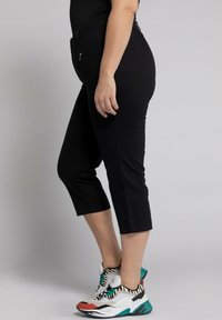 Pantaloni neri a vita alta, realizzati in un tessuto liscio ed elasticizzato, con un taglio slim, abbinati a sneakers bianche e turchesi.