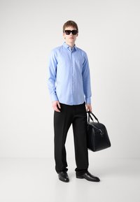 Camisa azul claro de botones, pantalones negros, zapatos pulidos negros y gafas de sol. Sosteniendo un bolso de cuero negro estructurado. Diseño simple y elegante.