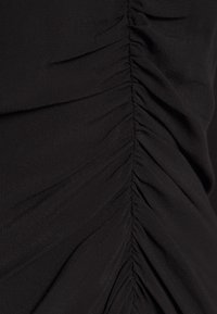 Gros plan sur un tissu noir avec un détail plissé le long d'une couture centrale créant des plis texturés.