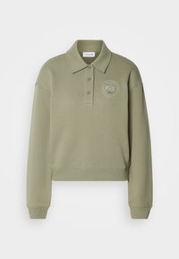 Sweat-shirt polo à manches longues vert clair avec trois boutons et logo rond Lacoste sur la poitrine gauche indiquant "Lacoste French Sportswear".