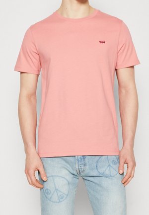Lyserød crew neck T-shirt lavet af bomuld med korte ærmer; har et lille rødt Levi's-logo på venstre bryst. Sammen med lyseblå jeans.
