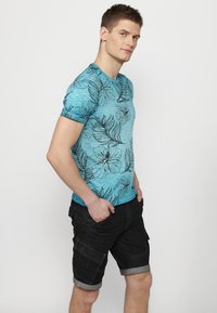 Gaiši zils īsās piedurknes T-krekls ar melnu ziedu apdruku, savienots ar tumšiem cargo šortiem ar rullētām piedurknēm un vairākiem kabatām.