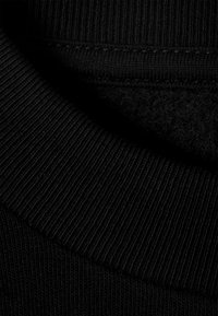 Juoda riboto megzto audinio su lygiu paviršiumi, apvali iškirptė ir matomi siūlių detalės.