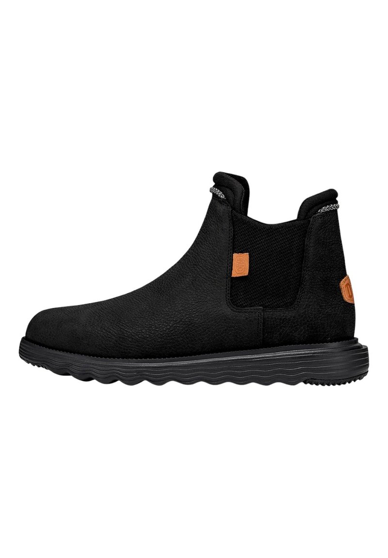 Botas chelsea negras con un acabado de ante texturizado, paneles laterales elásticos y una suela de goma en forma de sierra. Presenta una pequeña pestaña de acento naranja.