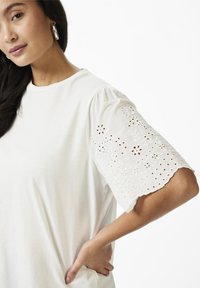 Tricou alb cu mâneci scurte volanate, cu broderie rafinată din eyelet și modele florale pe margine. Material moale, croi lejer.