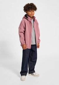 Rosa huvad jacka med elastiska muddar, bärs över en grå tröja, kombinerad med mörkblå jeans och vita sneakers med svarta ränder.