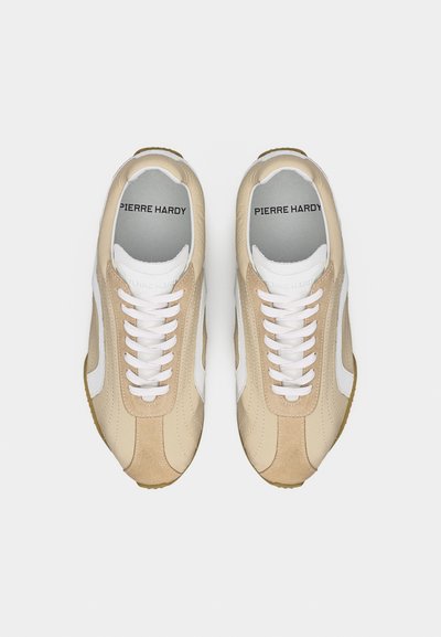 Paire de baskets Pierre Hardy beiges et blanches avec des lacets blancs, vues de dessus sur un fond gris uni.
