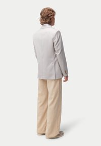 Blazer gris clair ajusté avec un col cranté et une fermeture à deux boutons, associé à un pantalon large plissé beige et des chaussures beige.