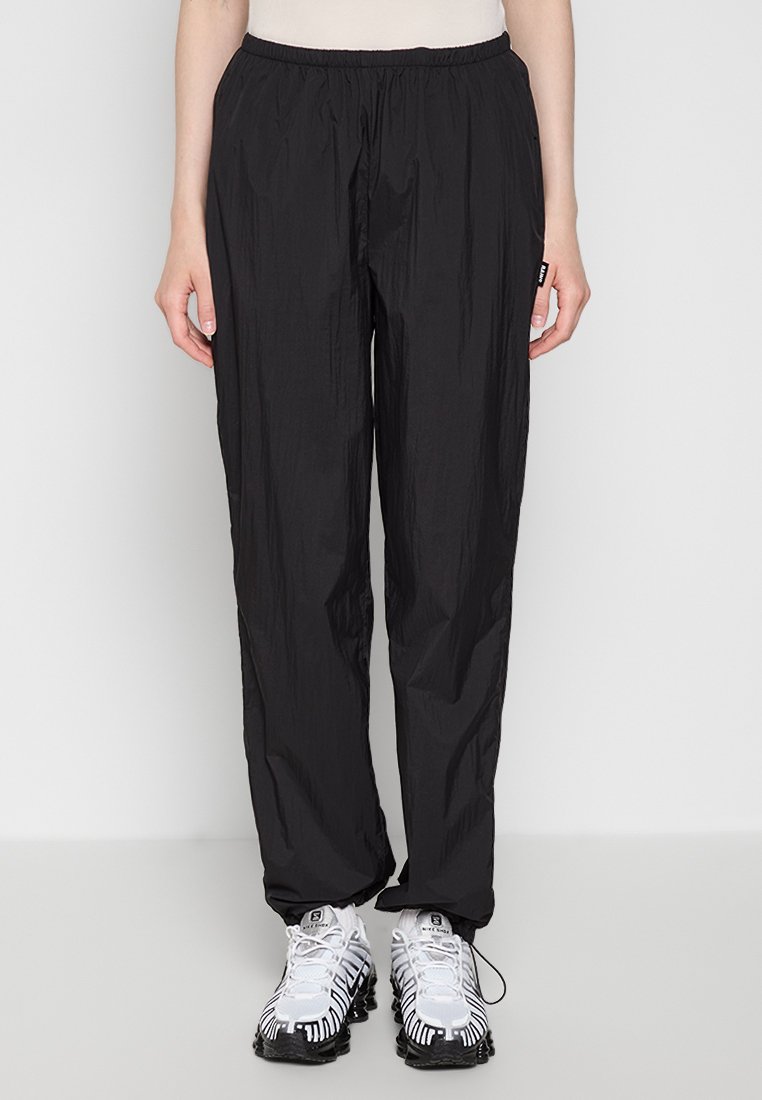 Schwarze, leichte Sport-Jogginghosen mit einem elastischen Bund, die eine glatte Textur und einen lockeren Schnitt aufweisen, kombiniert mit weißen und schwarzen gemusterten Schuhen.
