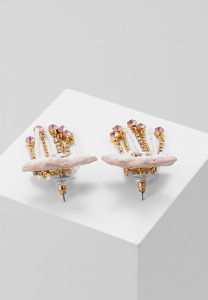 Pendientes de botón de oro con cuentas blancas, piedras preciosas rosas y pequeños cristales transparentes exhibidos sobre un pedestal blanco contra un fondo gris.