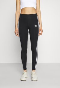 Svarta leggings med vita sidostråk och en broderad Adidas-logotyp. Tillverkade av elastiskt material med hög midja för komfort.