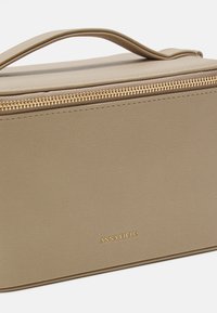 Beige faux leather cosmetic bag with a top handle, gold zipper, and embossed brand name. Rectangular shape with textured surface.