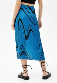 Sininen midi-hame, jossa on mustia aaltoilevia kuvioita, valmistettu sileästä kankaasta. Yhdistetty mustiin narusandaaleihin, joissa on paksu pohja.