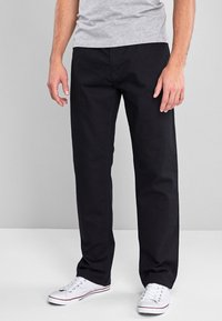 Schwarze Baumwollhose mit geraden Beinen, ausgestattet mit Taschen und einer glatten Textur, kombiniert mit weißen Sneakers und einem grauen Shirt.