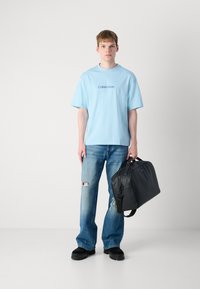Lys blå oversized t-skjorte med "Calvin Klein"-logo, slitt blå jeans og svart glatt lærveske. Arbeidssko med tykke såler.